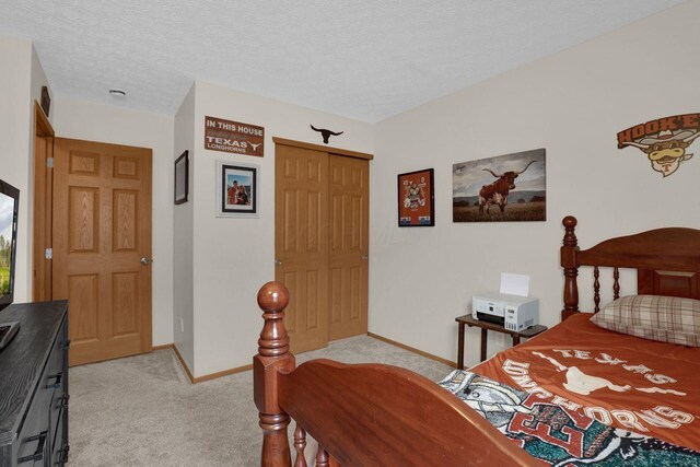 bedroom featuring light colored carpet, baseboards, and a textured ceiling