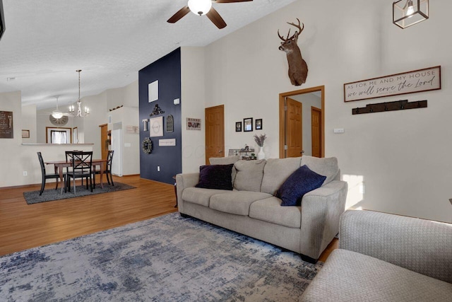 living area with ceiling fan with notable chandelier, high vaulted ceiling, wood finished floors, and a textured ceiling