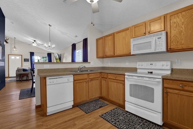 kitchen featuring white appliances, a peninsula, a sink, vaulted ceiling, and light wood-type flooring