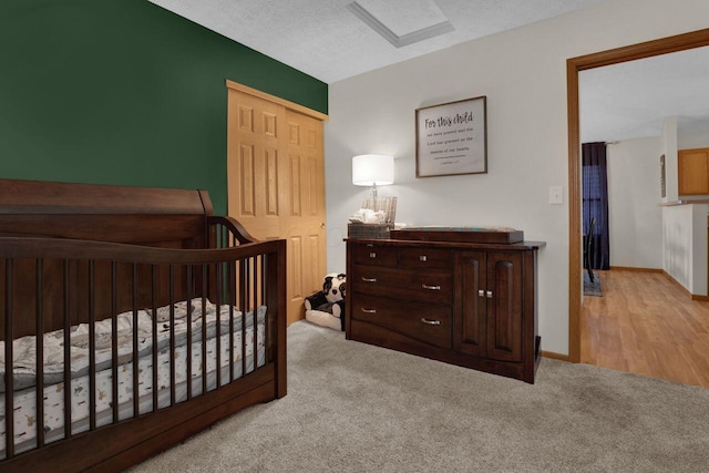 carpeted bedroom featuring a nursery area, baseboards, a closet, and a textured ceiling