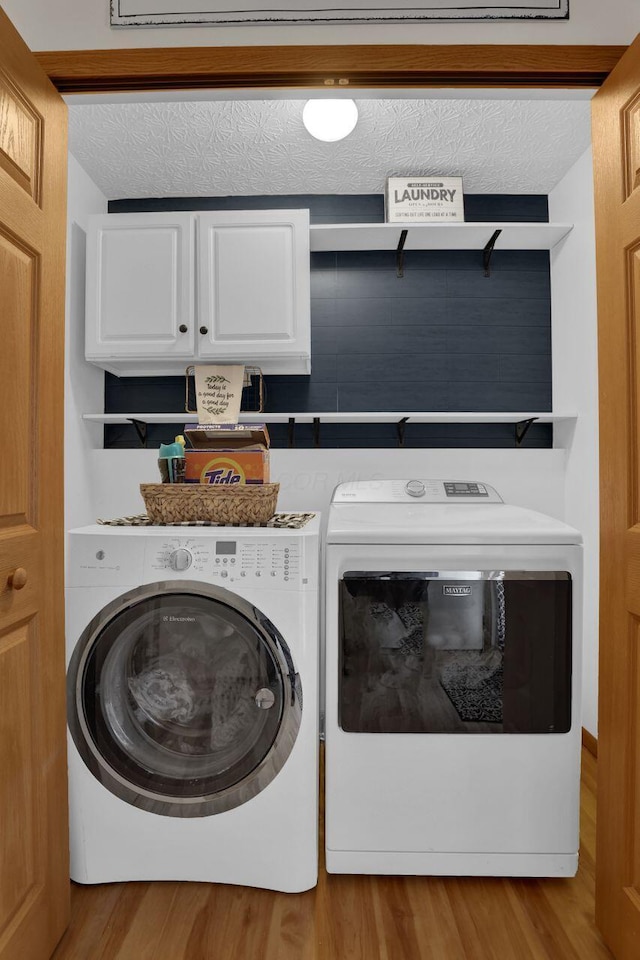 clothes washing area with washing machine and clothes dryer, cabinet space, a textured ceiling, and wood finished floors