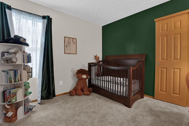 bedroom with a textured ceiling, baseboards, a nursery area, and carpet floors