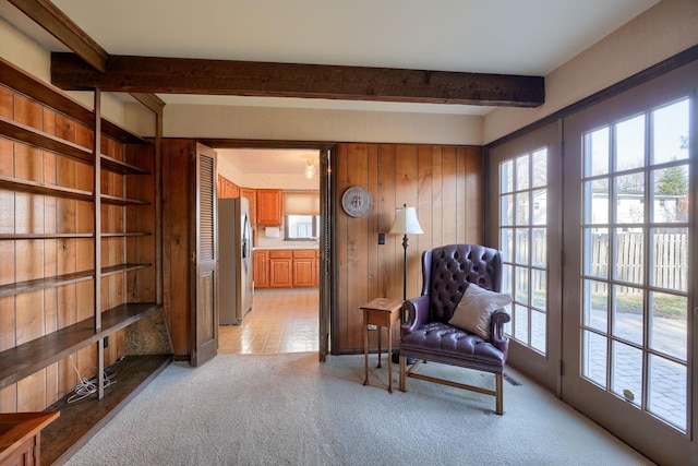 sitting room with beam ceiling, wooden walls, and light carpet