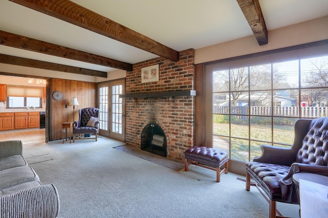 living area with wooden walls, a brick fireplace, wine cooler, light colored carpet, and beam ceiling