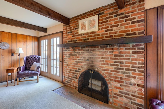 carpeted living area featuring beamed ceiling, a brick fireplace, and wood walls