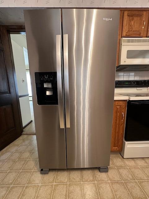 kitchen featuring white microwave, brown cabinets, electric stove, and stainless steel fridge with ice dispenser