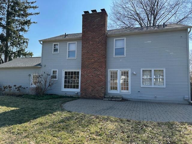 back of house featuring a lawn, a chimney, and a patio