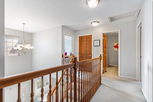 corridor featuring an upstairs landing, a notable chandelier, light carpet, baseboards, and attic access