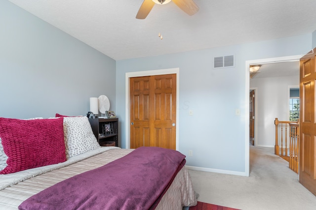 bedroom with visible vents, light carpet, a textured ceiling, baseboards, and ceiling fan