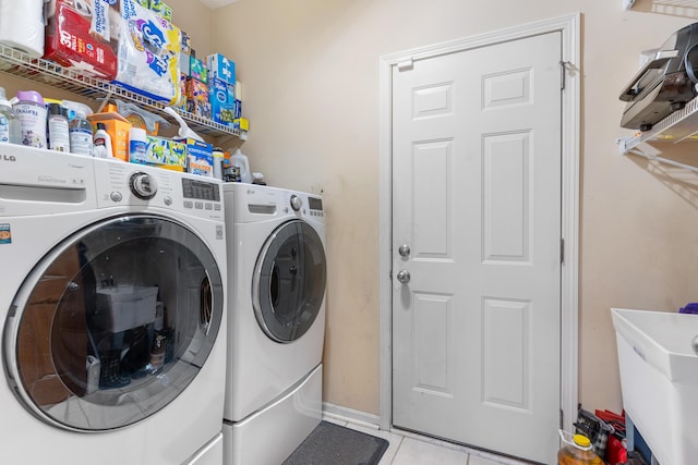 clothes washing area featuring a sink, separate washer and dryer, light tile patterned floors, baseboards, and laundry area