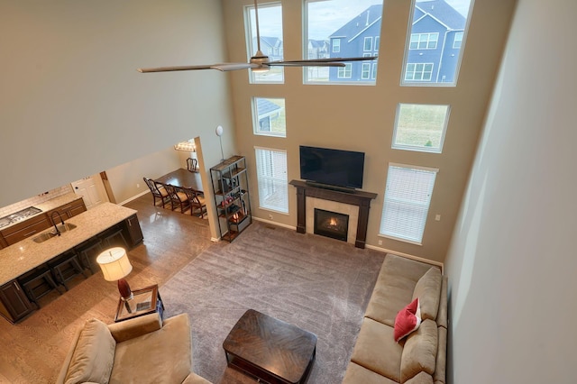 living area featuring a ceiling fan, baseboards, a high ceiling, a tiled fireplace, and carpet flooring