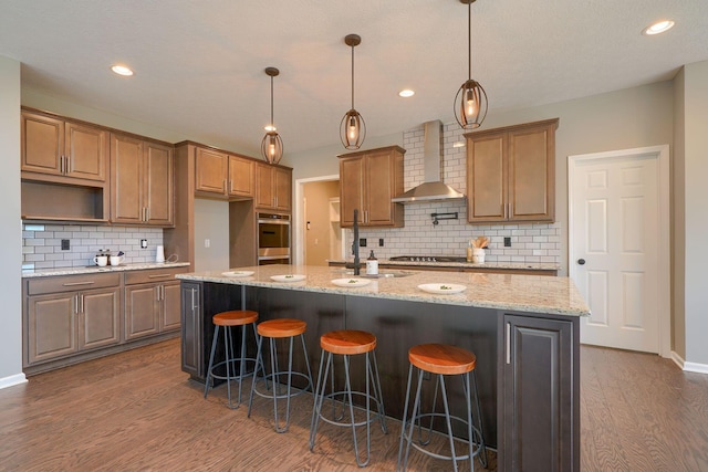 5511 Timber Heights Ln, Grove City, OH 43123 - kitchen with wall chimney range hood, dark wood-style flooring, a breakfast bar, decorative backsplash, and a center island with sink