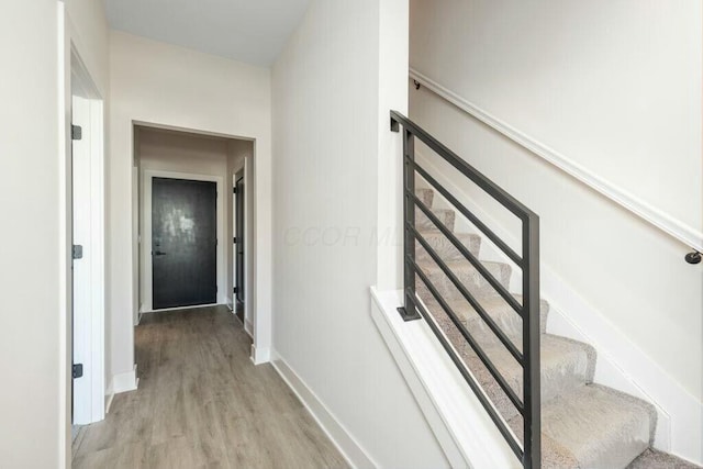 hallway featuring stairs, light wood-type flooring, and baseboards