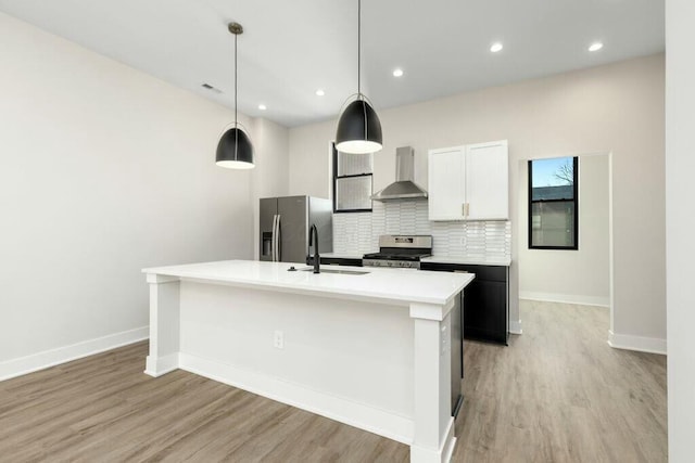 kitchen featuring a center island with sink, tasteful backsplash, light wood-style floors, appliances with stainless steel finishes, and wall chimney exhaust hood