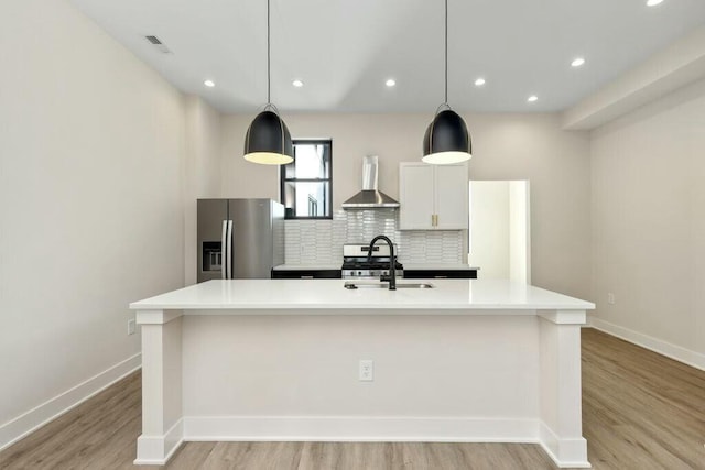 kitchen featuring visible vents, a sink, stainless steel refrigerator with ice dispenser, wall chimney range hood, and tasteful backsplash