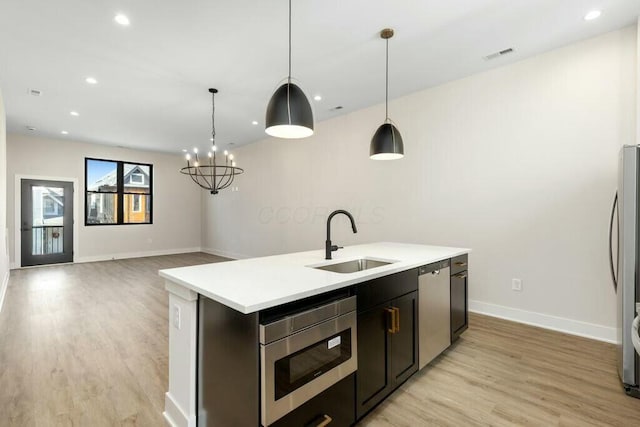 kitchen featuring visible vents, a sink, appliances with stainless steel finishes, light wood-style floors, and a kitchen island with sink