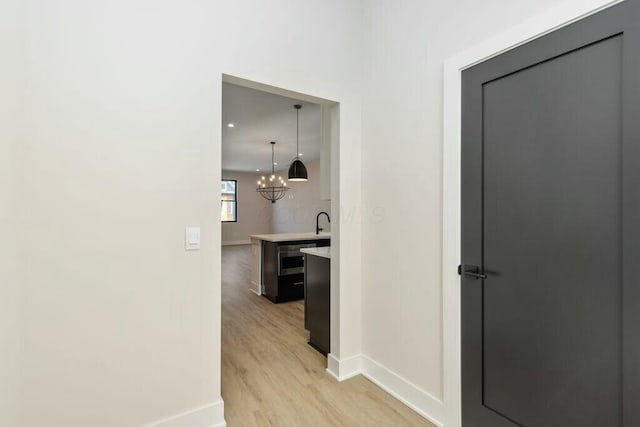 corridor with baseboards, a chandelier, and light wood finished floors