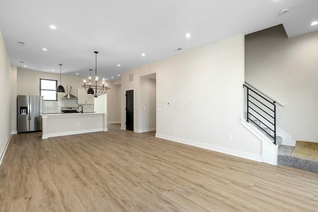 unfurnished living room with stairs, an inviting chandelier, recessed lighting, and light wood finished floors