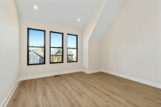 additional living space featuring vaulted ceiling, light wood-style flooring, baseboards, and visible vents