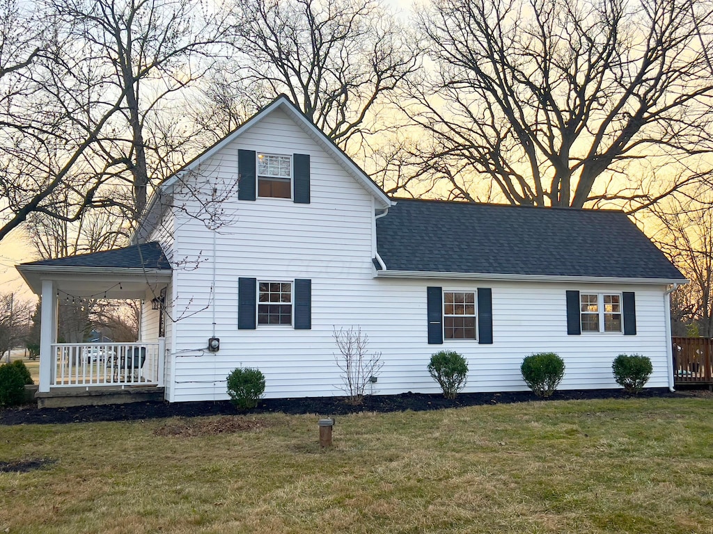 exterior space with a porch, a shingled roof, and a front lawn