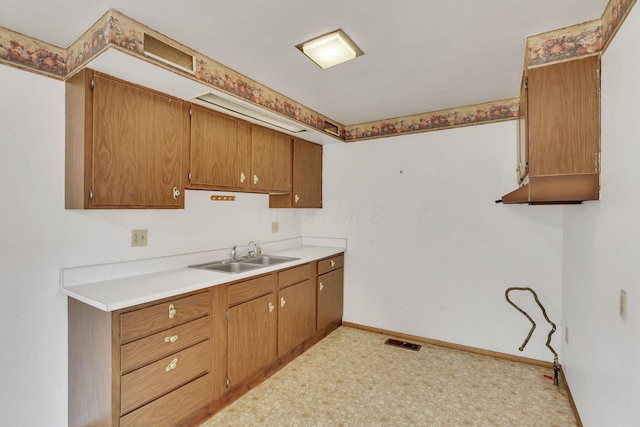 kitchen with visible vents, brown cabinets, a sink, light countertops, and baseboards