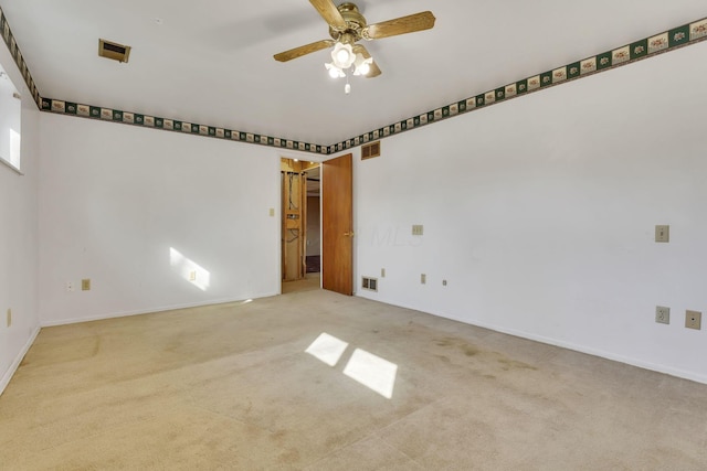 carpeted spare room with visible vents, baseboards, and ceiling fan