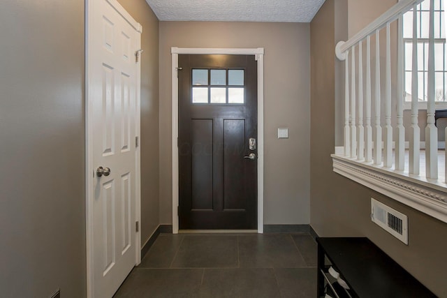 entrance foyer with visible vents, baseboards, a textured ceiling, and dark tile patterned floors