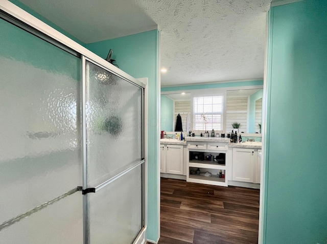 full bath with a shower stall, wood finished floors, double vanity, and a textured ceiling