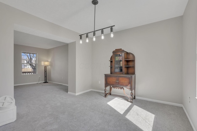 carpeted spare room featuring rail lighting and baseboards