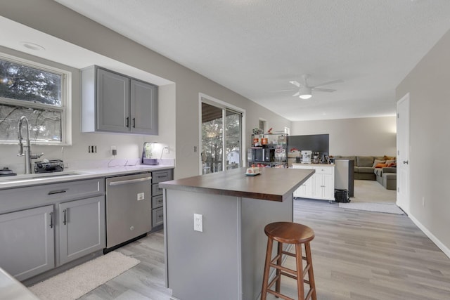 kitchen featuring a ceiling fan, gray cabinets, a sink, a kitchen breakfast bar, and stainless steel dishwasher