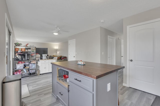 kitchen with light wood finished floors, butcher block countertops, open floor plan, white cabinetry, and a ceiling fan