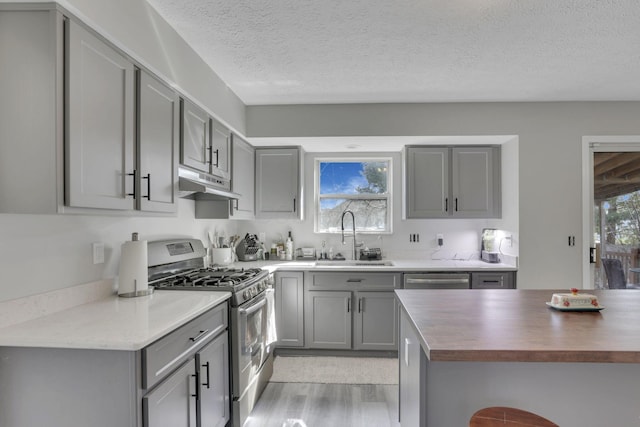 kitchen featuring gray cabinetry, under cabinet range hood, stainless steel range with gas stovetop, plenty of natural light, and a sink