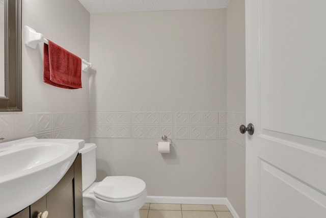 bathroom featuring toilet, a textured ceiling, tile walls, wainscoting, and tile patterned flooring