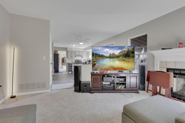 living room featuring ceiling fan, a tile fireplace, visible vents, and light carpet