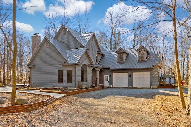 view of front facade with a chimney, metal roof, gravel driveway, and a garage