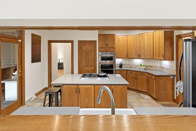 kitchen with stainless steel appliances, a kitchen island, a breakfast bar area, and brown cabinetry