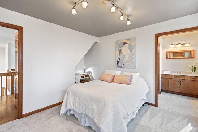 bedroom with light carpet, ensuite bath, and baseboards