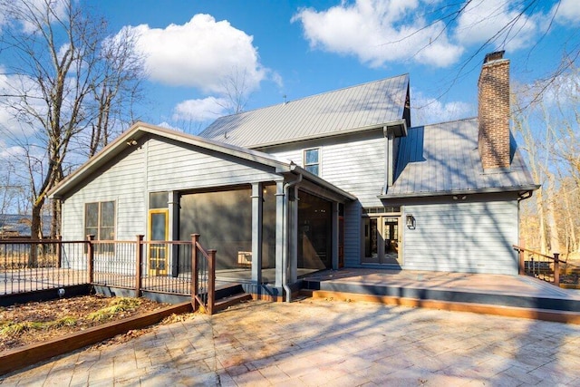 back of property with a deck, a sunroom, and a chimney