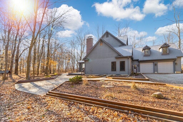 view of home's exterior featuring metal roof, gravel driveway, a chimney, and an attached garage