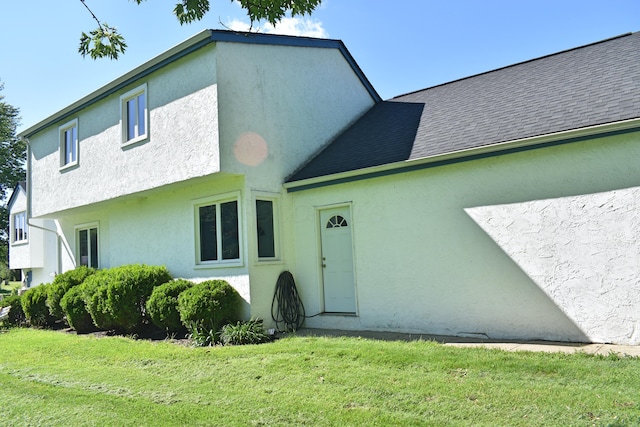 view of front of home featuring stucco siding, a front lawn, and roof with shingles