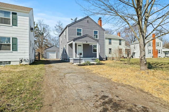 view of front facade with a detached garage, aphalt driveway, a front yard, covered porch, and an outdoor structure