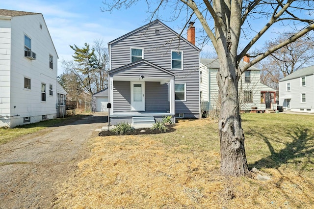 traditional-style house featuring a porch, a chimney, an outdoor structure, a front lawn, and a garage