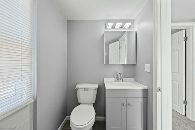 half bathroom featuring baseboards, toilet, and vanity