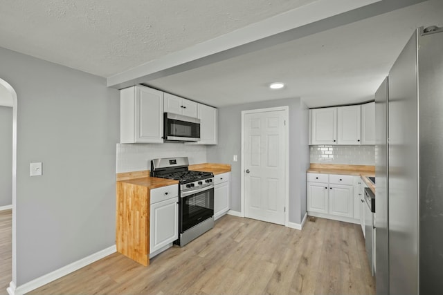 kitchen featuring butcher block countertops, light wood-type flooring, arched walkways, and appliances with stainless steel finishes