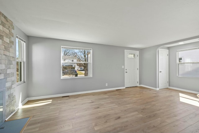 unfurnished living room featuring visible vents, wood finished floors, arched walkways, a stone fireplace, and baseboards