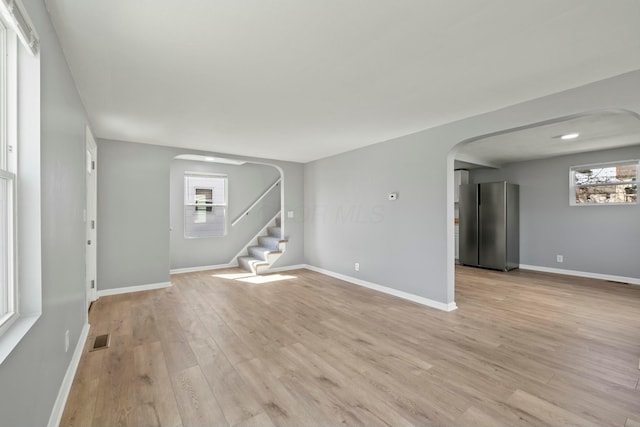 unfurnished living room featuring arched walkways, baseboards, stairs, and light wood-style floors