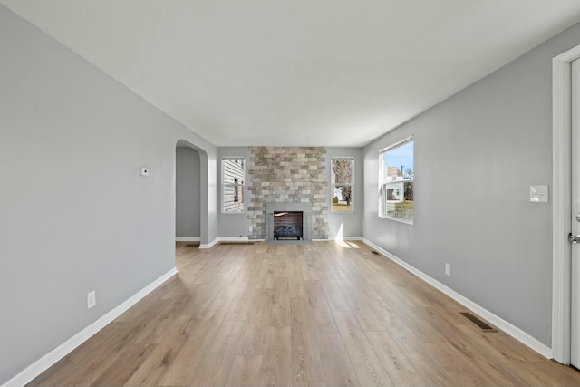 unfurnished living room featuring a wealth of natural light, visible vents, light wood-type flooring, and arched walkways