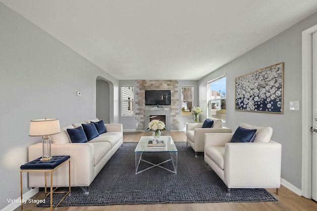 living area featuring arched walkways, a fireplace, baseboards, and wood finished floors