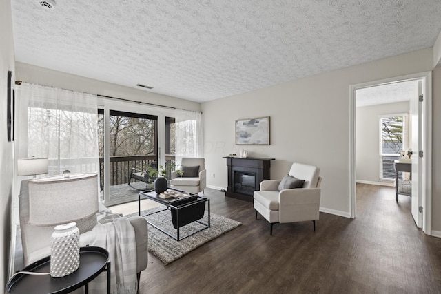 living area featuring baseboards, a textured ceiling, visible vents, a glass covered fireplace, and wood finished floors