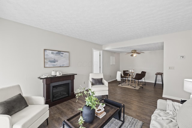 living room featuring baseboards, a textured ceiling, wood finished floors, and a glass covered fireplace